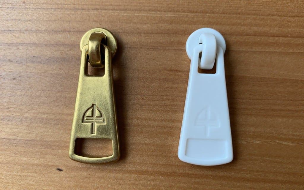 Side-by-side comparison of authentic brass zipper hardware with crisp logo engraving versus counterfeit plastic hardware with blurry impression