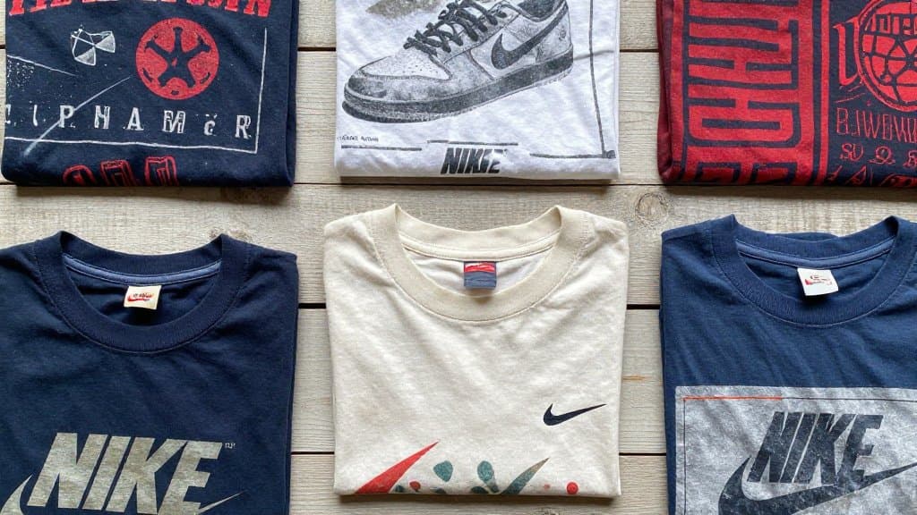Vintage 80s and Nike single stitch t shirts laid out on wood for resale sorting