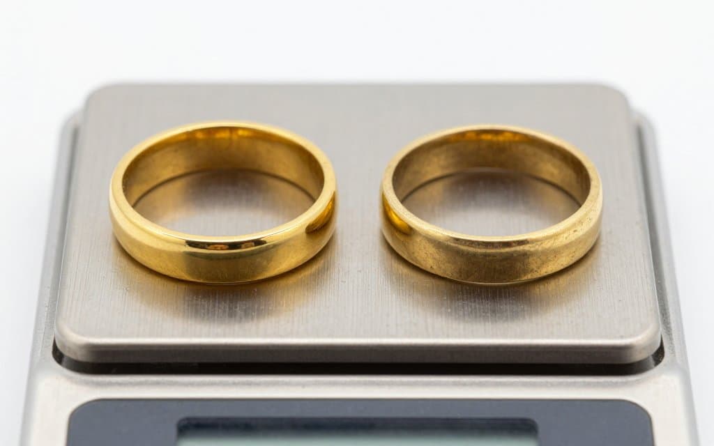 Two gold rings on a scale comparing solid gold with plated brass value