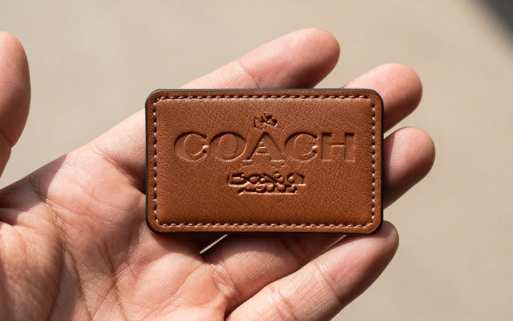 Close-up of coach date codes stamped into a leather creed patch, letters and digits clearly visible