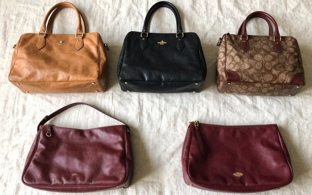 Flat lay of several vintage coach bags in different colors and eras arranged on a linen surface