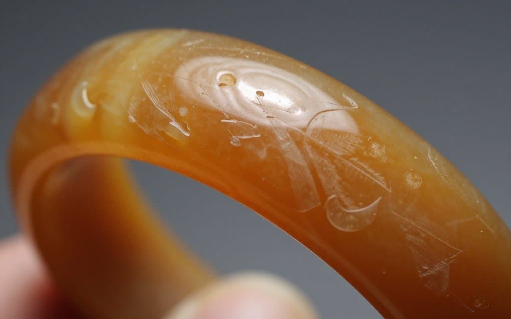 Macro view of a carved butterscotch bakelite bangle showing hand carved detail.