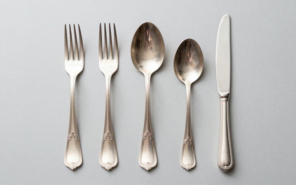 Top down view of a matched sterling silver flatware place setting showing the ornate pattern on each handle
