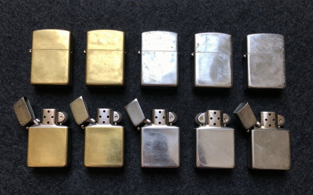 A flat lay of several vintage Zippo lighters in different finishes showing age and wear.