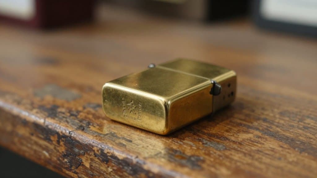 A vintage brass Zippo lighter face down showing its bottom date stamp on a wooden thrift counter.