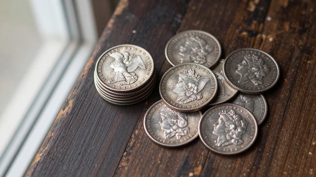 A pile of antique Morgan and Peace silver dollars on dark wood, a find that can range in value from melt to thousands of dollars