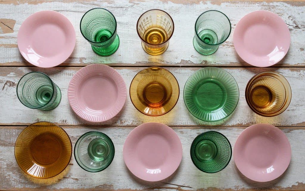Top-down arrangement of pastel depression glass plates and bowls on a wood table