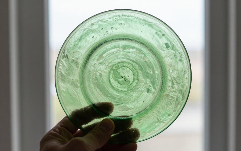 Hand holding depression glass to the light to check bubbles and authenticity
