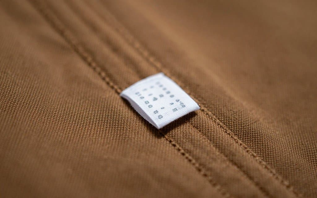 Macro view of a care tag inside a canvas jacket, where Carhartt tags by year show the production date